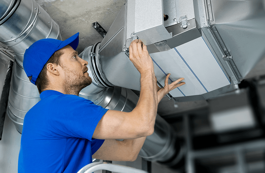 Technician adjusting overhead ductwork for industrial air conditioner repair in Raleigh, NC